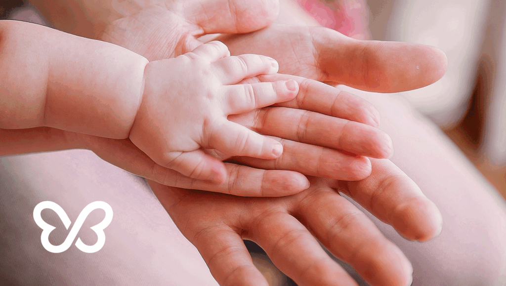 Close-up of a baby’s small hand resting on top of an adult’s hand, symbolizing love, care, and the journey of family through surrogacy or adoption.